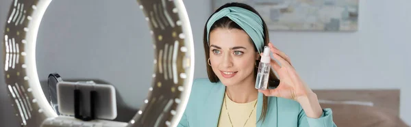 Teléfono inteligente borroso en titular con lámpara de anillo cerca de blogger belleza con agua micelar, pancarta — Stock Photo