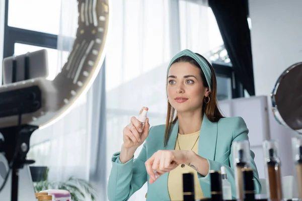 Titular de teléfono borroso con luz de anillo cerca de belleza blogger aplicación de agua micelar en la mano — Stock Photo