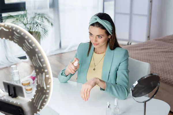 Joven blogger de belleza aplicando agua micelar a mano cerca del soporte del teléfono con luz circular — Stock Photo