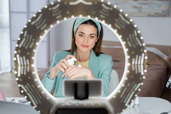 Blurred phone holder with circle light near beauty blogger applying face foam on hand — Stock Photo