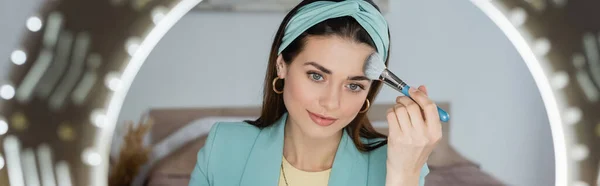 Stylish beauty blogger applying face powder near ring light, banner — Stock Photo