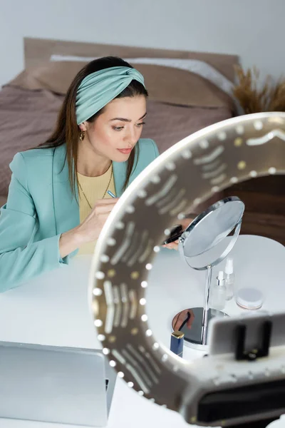 Elegante beauty blogger vicino specchio, laptop e portatelefono con luce circolare — Foto stock