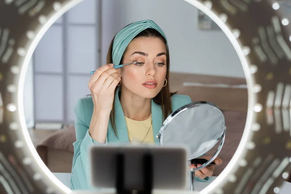 Blurred smartphone in phone holder with ring light near beauty blogger applying eye shadows — Stock Photo