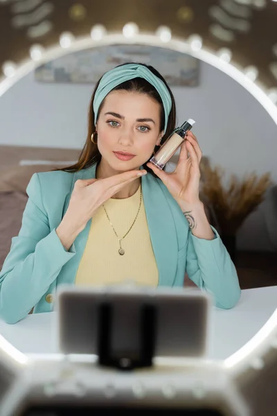 Blurred phone holder with circle lamp near beauty blogger showing face foundation — Stock Photo