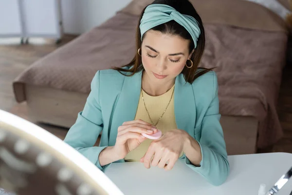 Stylish beauty blogger using cosmetic sponge on hand near ring light — Stock Photo