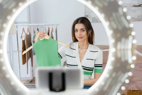 Blurred phone holder with circle lamp near fashion blogger showing vest on holder — Stock Photo