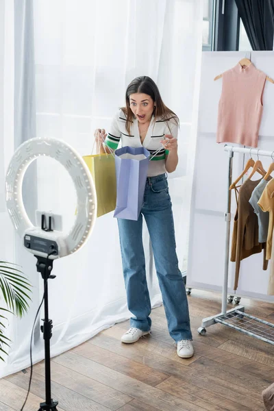 Erstaunt Modebloggerin hält Einkaufstaschen in der Nähe von Handyhalterung mit Kreislicht — Stockfoto