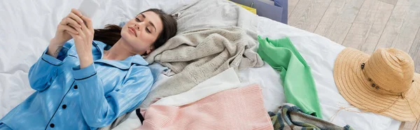 Positive Frau, die in der Nähe von Kleidung auf dem Bett liegt und Videobotschaften mit dem Handy aufzeichnet, Banner — Stockfoto