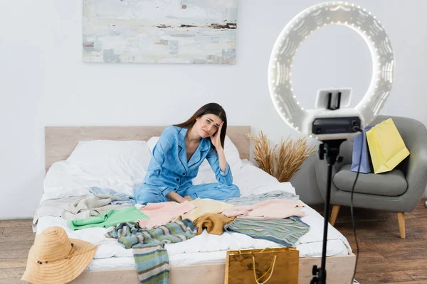 Upset woman near assortment of clothes and phone holder with circle lamp — Stock Photo