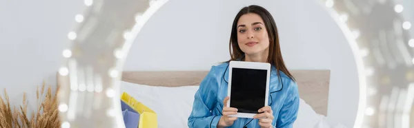 Blogueur de mode joyeux en pyjama élégant montrant tablette numérique près de la lumière du cercle floue, bannière — Photo de stock