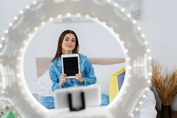 Titular de teléfono borroso con lámpara de anillo cerca de blogger de moda en pijama elegante celebración tableta digital — Stock Photo