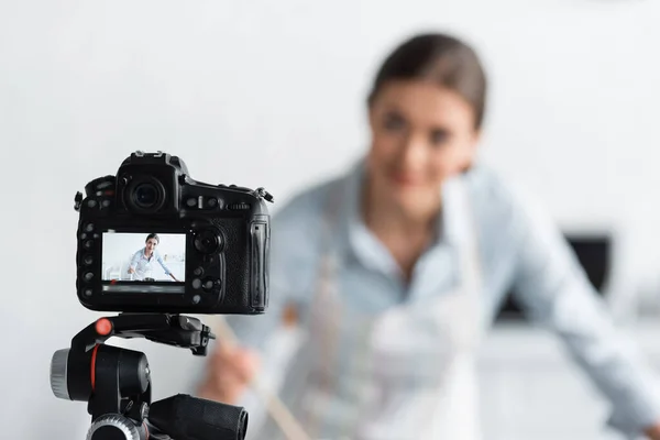 Selective focus of digital camera near blurred culinary blogger in kitchen — Stock Photo