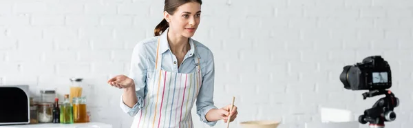 Joven blogger culinario apuntando con la mano cerca de la cámara digital en la cocina, pancarta - foto de stock