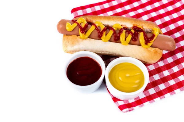 Taças com mostarda e ketchup perto de cachorro-quente saboroso em guardanapo de mesa xadrez isolado em branco — Fotografia de Stock