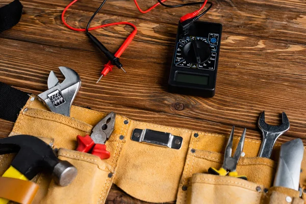 Voltmeter near leather belt with different tools on wooden surface, labor day concept — Stock Photo