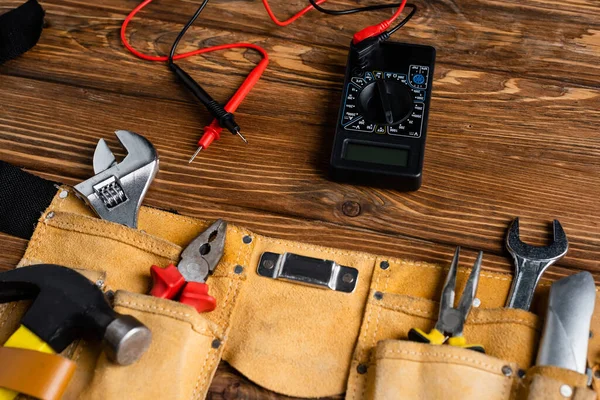 Voltmetro vicino alla cintura di cuoio con diversi strumenti sulla superficie di legno, concetto di giornata lavorativa — Foto stock