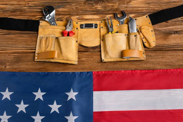 Draufsicht auf usa flag near leather tool belt mit verschiedenen werkzeugen auf holzoberfläche, labor day concept — Stockfoto