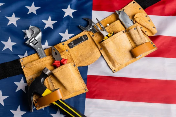 Vista superior del cinturón de herramientas de cuero con varias herramientas en la bandera americana, concepto del día del trabajo - foto de stock