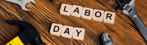 Cubes with labor day lettering near various tools on wooden surface, banner — Stock Photo