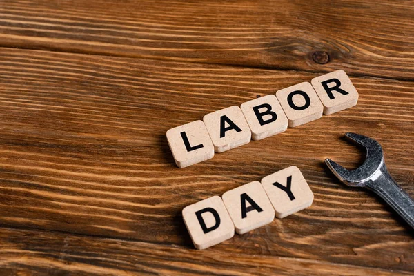 Llave inglesa cerca de cubos con letras del día del trabajo en la mesa de madera - foto de stock