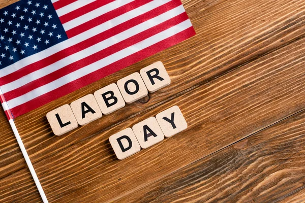 Top view of cubes with labor day lettering near small usa flag on wooden table — Stock Photo