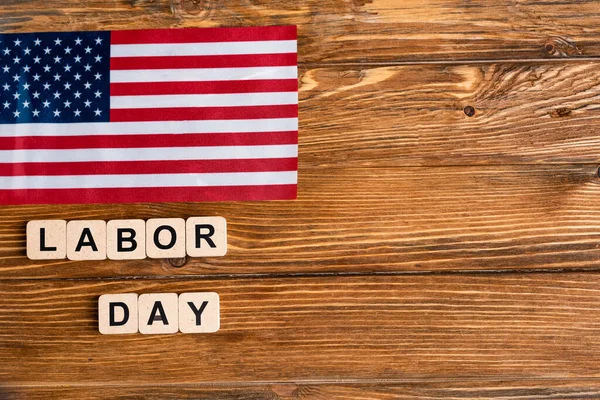 Верхний вид флага США рядом с кубиками с надписью Дня труда на деревянном столе — стоковое фото