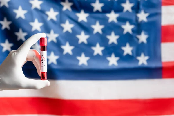 Partial view of person in latex glove holding positive coronavirus test near blurred american flag — Stock Photo