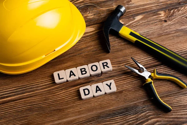 Helmet, hammer, pliers and cubes with labor day lettering on wooden surface — Stock Photo