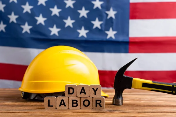 Cubes with labor day lettering, hammer and hardhat near usa flag on blurred background — Stock Photo