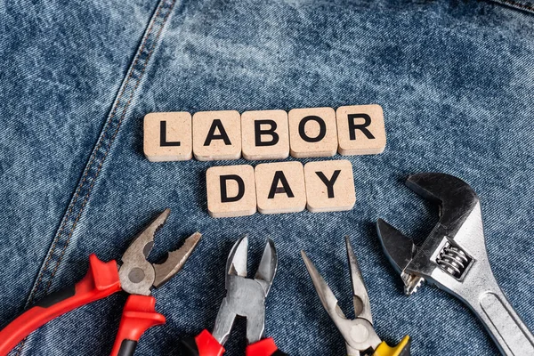 Top view of wooden cubes with labor day lettering near tools on blue denim cloth — Stock Photo