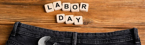 Vista superior de la llave inglesa y jeans cerca de cubos con letras del día del trabajo en la mesa de madera, bandera - foto de stock