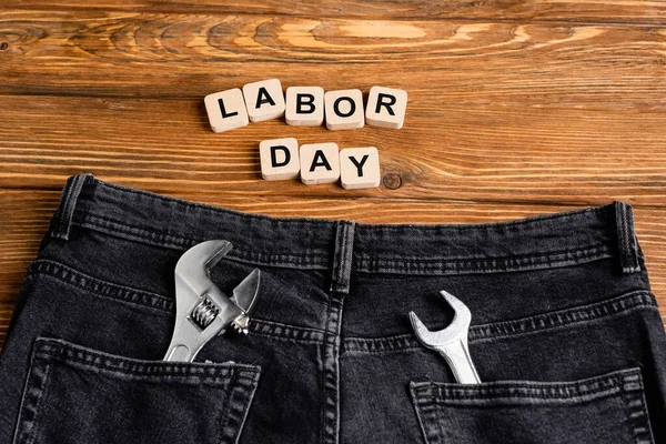 Top view of jeans with wrenches in back pockets near cubes with labor day lettering on wooden table — Stock Photo