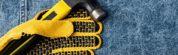 Вид зверху молотка біля жовтих прогумованих робочих рукавичок на джинсовій тканині, концепція робочого дня, банер — стокове фото