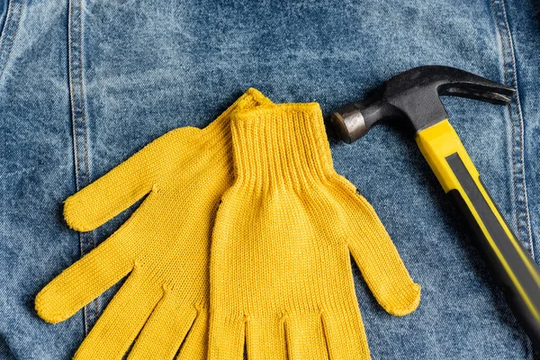 Vista dall'alto di guanti da lavoro gialli vicino martello su tessuto denim blu, concetto di giorno di lavoro — Foto stock