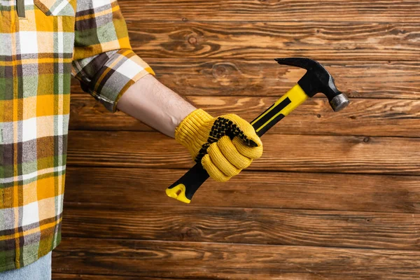 Vista parcial del manitas en guante de trabajo sosteniendo hummer sobre fondo de madera, concepto del día del trabajo - foto de stock