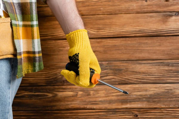 Partial view of handyman in work glove holding screwdriver on wooden background, labor day concept — Stock Photo