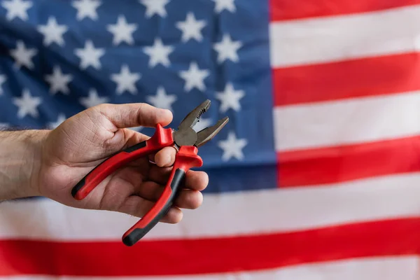 Partial view of workman holding pliers near blurred usa flag, labor day concept — Stock Photo