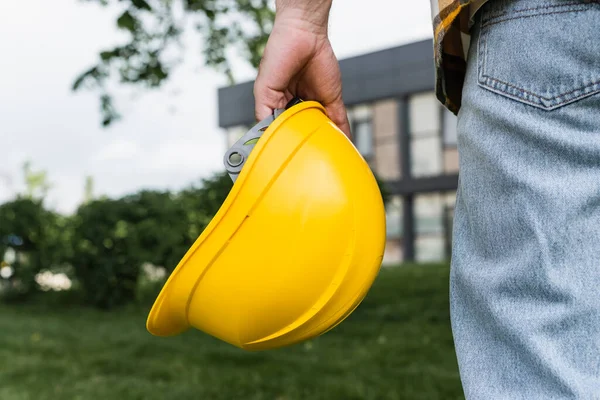 Visão cortada do trabalhador segurando hardhat ao ar livre, conceito de dia de trabalho — Fotografia de Stock