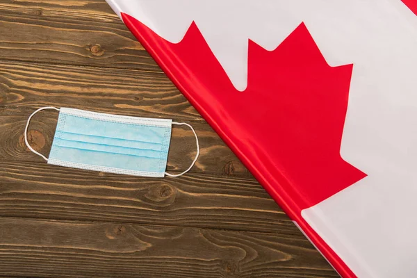 Vista superior de la bandera canadiense y máscara médica en la superficie de madera, concepto covid-19 - foto de stock