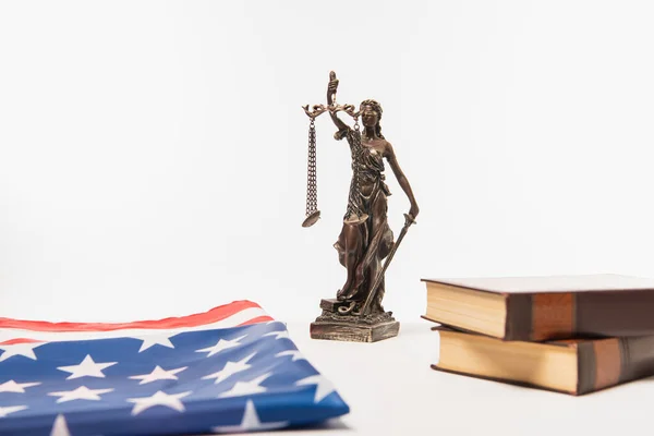 Estatuilla de justicia cerca de bandera americana y libros aislados en blanco - foto de stock