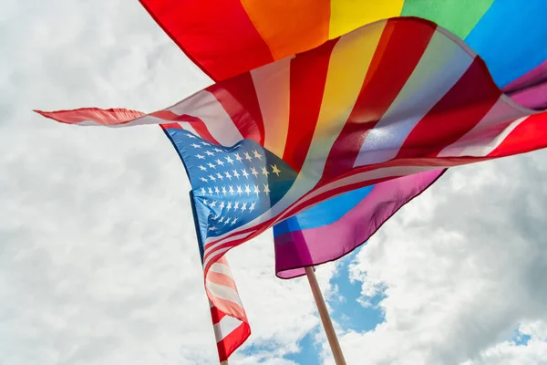 Bottom view of american and colorful lgbt flags against sky — Stock Photo