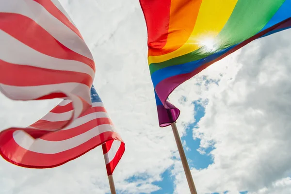 Blick von unten auf amerikanische und bunte lgbt-Flaggen gegen wolkenverhangenen Himmel — Stockfoto