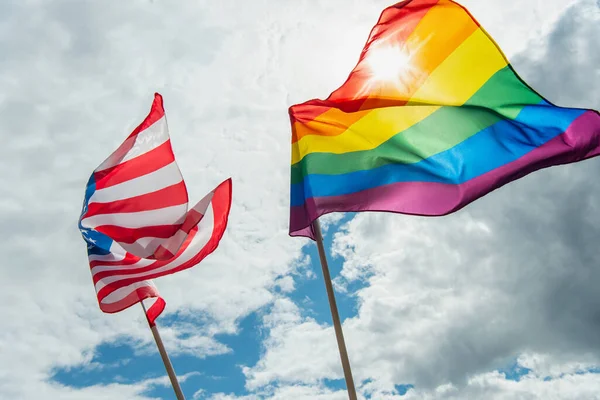 Low angle view of american and colorful lgbt flags against blue sky with clouds — Stock Photo