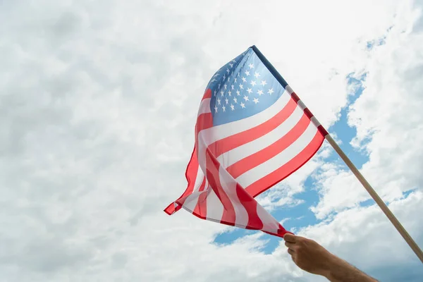 Cropped view of man holding american flag with stars and stripes against cloudy sky — Stock Photo