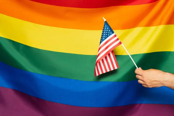 Recortado vista de hombre sosteniendo bandera americana contra lgbt colorido fondo - foto de stock