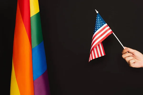 Vista recortada del hombre sosteniendo la bandera de América cerca de lgbt tela colorida aislada en negro - foto de stock