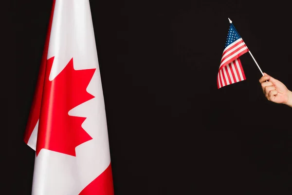 Vista recortada del hombre sosteniendo la bandera americana cerca del símbolo canadiense aislado en negro - foto de stock