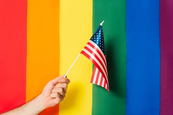 Vista cortada do homem segurando bandeira da América contra lgbt fundo colorido — Fotografia de Stock