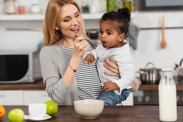 Alegre madre alimentación adoptado africano americano hija - foto de stock