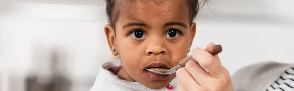 Mãe segurando colher e alimentação adotada afro-americana filha, banner — Fotografia de Stock